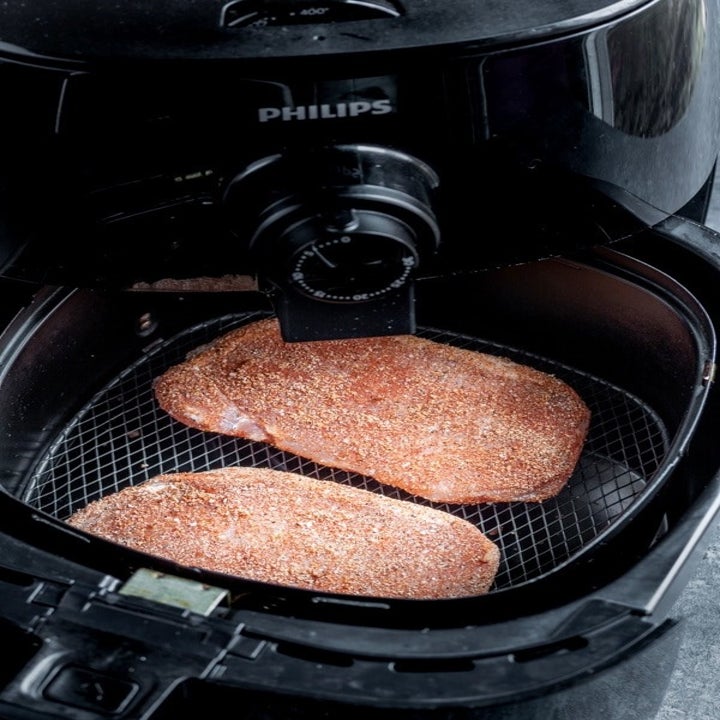 Two pork chops in the basket of an air fryer.